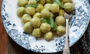 Piatto di gnocchi di zucchine fatti in casa, conditi con burro e salvia, su un piatto decorato con fiori blu.