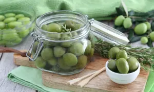 Verdi olive in salamoia per olive, conservate in un barattolo di vetro con rametti di rosmarino.
