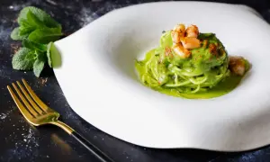 Spaghetti di zucchine con gamberi e salsa verde, guarniti con paprika e menta fresca. Un piatto leggero e colorato.