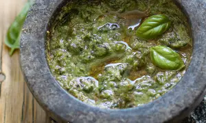 Mortai con pestello pieno di profumato pesto alla genovese, guarnito con foglie di basilico fresco.