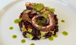 Delizioso polpo alla griglia servito su riso venere con avocado e pomodorini, guarnito con salsa verde.