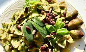 Farfalle condite con un saporito pesto di salvia, guarnite con pistacchi, basilico e olive verdi.