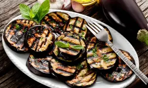 Melanzane grigliate su un piatto bianco, condite con erbe aromatiche. Un invito a scoprire i 100 modi per cucinare le melanzane.