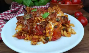 Piatto di pasta con pomodori al forno alla pugliese, filante e saporita, guarnita con basilico fresco.