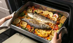 Due pesci interi, pronti per essere serviti, adagiati su un letto di verdure colorate e limone in una teglia. Un delizioso tonnetto al forno in preparazione.