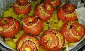 Pomodori ripieni di riso, cotti al forno su un letto di patate e erbe aromatiche. Un piatto saporito e colorato.