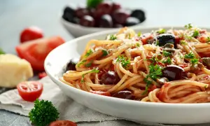 Spaghetti al sugo alla puttanesca, con pomodoro, olive, capperi e prezzemolo fresco, guarniti con parmigiano grattugiato.