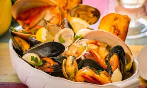 Un invitante piatto di zuppa di crostacei, ricco di cozze, vongole e gamberi, guarnito con limone e pane tostato.