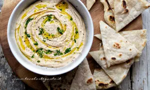 Delizioso hummus di fagioli cremoso, condito con olio d'oliva, prezzemolo e semi di sesamo, servito con pane pita tostato.