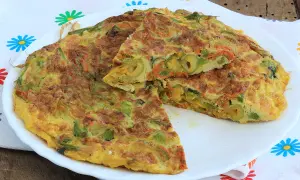 Frittata con fiori di zucca, carote e olive, tagliata a spicchi su un piatto bianco, con un tovagliolo colorato sullo sfondo.