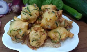 Frittelle di zucchine dorate e croccanti, pronte per essere gustate. Sullo sfondo, ingredienti freschi come basilico e cipolle rosse.