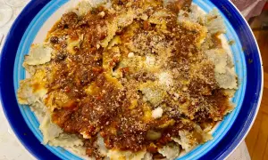 Piatto di ravioli alla genovese con sugo ricco e abbondante parmigiano grattugiato, serviti in un piatto blu e bianco.