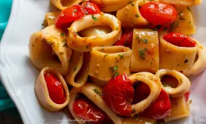 Piatto di calamarata ricetta originale con calamari e pomodorini freschi, guarnito con prezzemolo tritato.