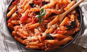 Piatto invitante di pasta con melanzane e pomodorini, condita con formaggio grattugiato e basilico fresco.