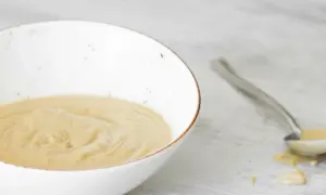 Una ciotola bianca contiene una cremosa salsa tonnata, con un cucchiaio che ne raccoglie una porzione.