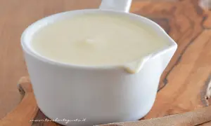 Una cremosa besciamella pronta per la tua ricetta, servita in una ciotolina bianca su un tagliere di legno.