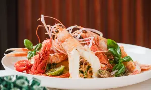 Un'appetitosa catalana di crostacei, con scampi, gamberi, pomodorini e basilico fresco, servita su un piatto bianco.