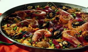 Un'abbondante paella valenciana in una padella, ricca di gamberi, cozze, piselli e pezzi di carne.