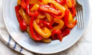 Peperoni in agrodolce, un contorno colorato e saporito, servito su un piatto azzurro con forchetta.