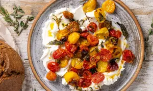 Pomodorini al forno succosi e colorati su una base cremosa, guarniti con erbe aromatiche. Perfetti con pane rustico.