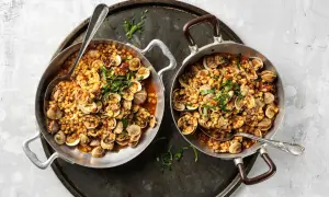 Due padelle piene di fregola con vongole, un piatto sardo profumato, guarnito con prezzemolo fresco.