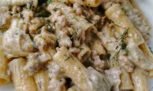 Primo piatto cremoso di pasta con tenerumi e ragù bianco, guarnito con aneto fresco.