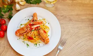 Un piatto di linguine con scampi, pomodorini e prezzemolo, uno dei migliori primi di pesce, pronto per essere gustato con un bicchiere di vino bianco.
