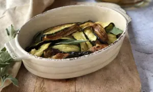 Zucchine in carpione dorate e saporite, guarnite con foglie di salvia fresca, servite in una ciotola di ceramica.
