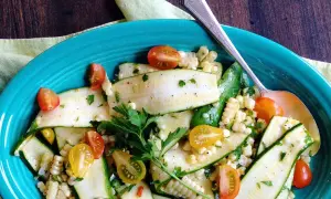 Insalata estiva con zucchine crude a fette, mais e pomodorini ciliegino, guarnita con prezzemolo fresco.