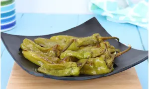 Friggitelli al forno, verdi e lucidi, serviti su un piatto nero. Un contorno saporito e facile da preparare.