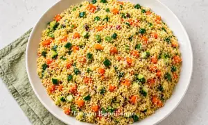 Un piatto invitante di cous cous con verdure colorate: carote, zucchine e cipolla rossa, pronto per essere gustato.
