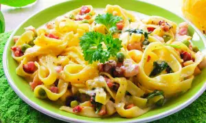 Un piatto di fettuccine cremose con piselli, pancetta e spinaci, un classico dei primi piatti pasquali.