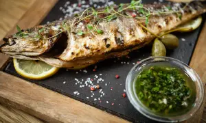 Un succulento branzino al forno, guarnito con erbe aromatiche, limone e capperi, accompagnato da una salsa verde.