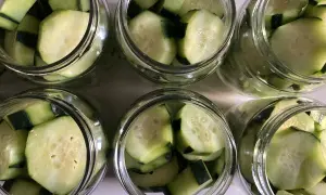 Sei barattoli di vetro pieni di **cetrioli sottaceto** tagliati a pezzi.