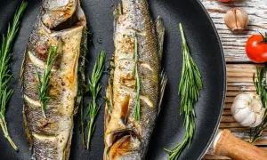 Due branzini interi cotti in padella, guarniti con rosmarino e limone. Perfetti per le tue branzino ricette.