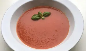 Una ciotola bianca contiene una vellutata salsa di pomodoro classica, guarnita con foglie di basilico fresco.