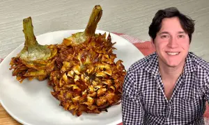 Due carciofi alla giudia dorati e croccanti su un piatto bianco, accanto a un uomo sorridente.