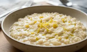 Un cremoso riso al limone, guarnito con scaglie di parmigiano e scorza di limone, pronto per essere gustato.
