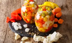 Due barattoli di giardiniera fatta in casa, pieni di verdure colorate come peperoni, carote e cavolfiore, pronti per essere gustati.