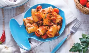 Piatto di pasta con calamaretti, pomodorini e prezzemolo su un piatto a forma di pesce blu.