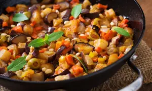 Caponata di verdure in padella, con melanzane, carote, olive e pinoli, guarnita con foglie di basilico fresco.
