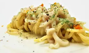 Un piatto di tonnarelli pasta conditi con una cremosa salsa bianca, guarniti con prezzemolo tritato e scorza d'arancia.