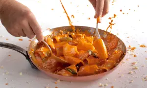 Mani che mescolano paccheri alla Vittorio in padella, con salsa arancione che schizza.