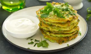 Frittelle dorate di zucchine trombetta, guarnite con prezzemolo fresco, servite con una ciotola di panna acida.