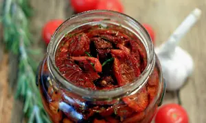Un barattolo pieno di pomodori secchi sott'olio, un assaggio della ricetta pomodori secchi sott'olio pugliese, con aglio e rosmarino.