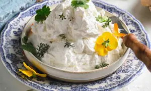 Burro montato soffice e arioso, guarnito con erbe aromatiche e fiori gialli, servito in una ciotola decorata.
