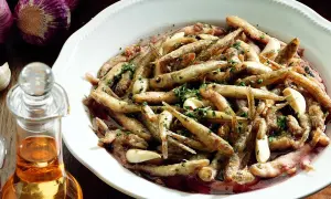 Un saporito carpione piemontese in un piatto bianco, condito con aglio e prezzemolo, accanto a una bottiglia d'olio e aglio viola.