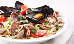 Un piatto invitante di tagliolini ai frutti di mare, con cozze, vongole e pomodorini freschi, guarnito con prezzemolo.