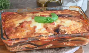 Parmigiana di melanzane non fritte, appena sfornata in teglia di vetro, con basilico fresco.