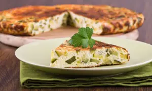 Una fetta di frittata di zucchine, soffice e dorata, guarnita con prezzemolo fresco, su un piatto chiaro.